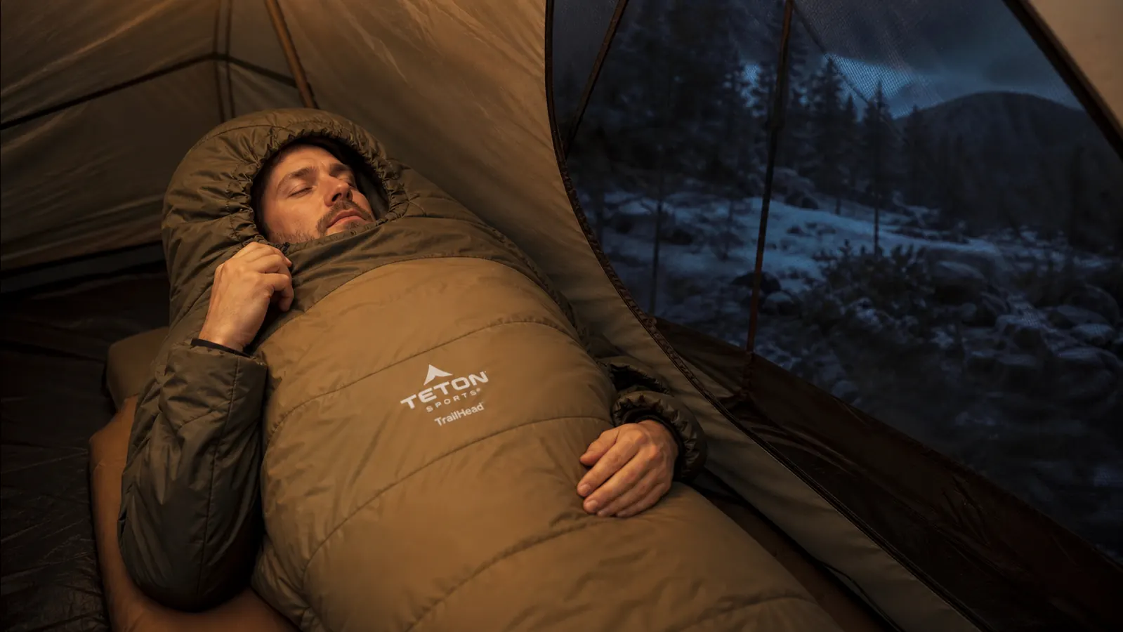 Camper pulling the mummy bag hood drawstring tight around their face with only nose and eyes visible in cold morning air