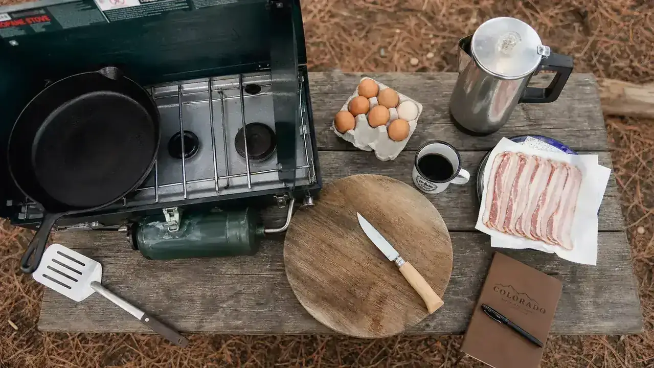 Six people seated at camp chairs around a picnic table, plates of eggs and pancakes in front of them