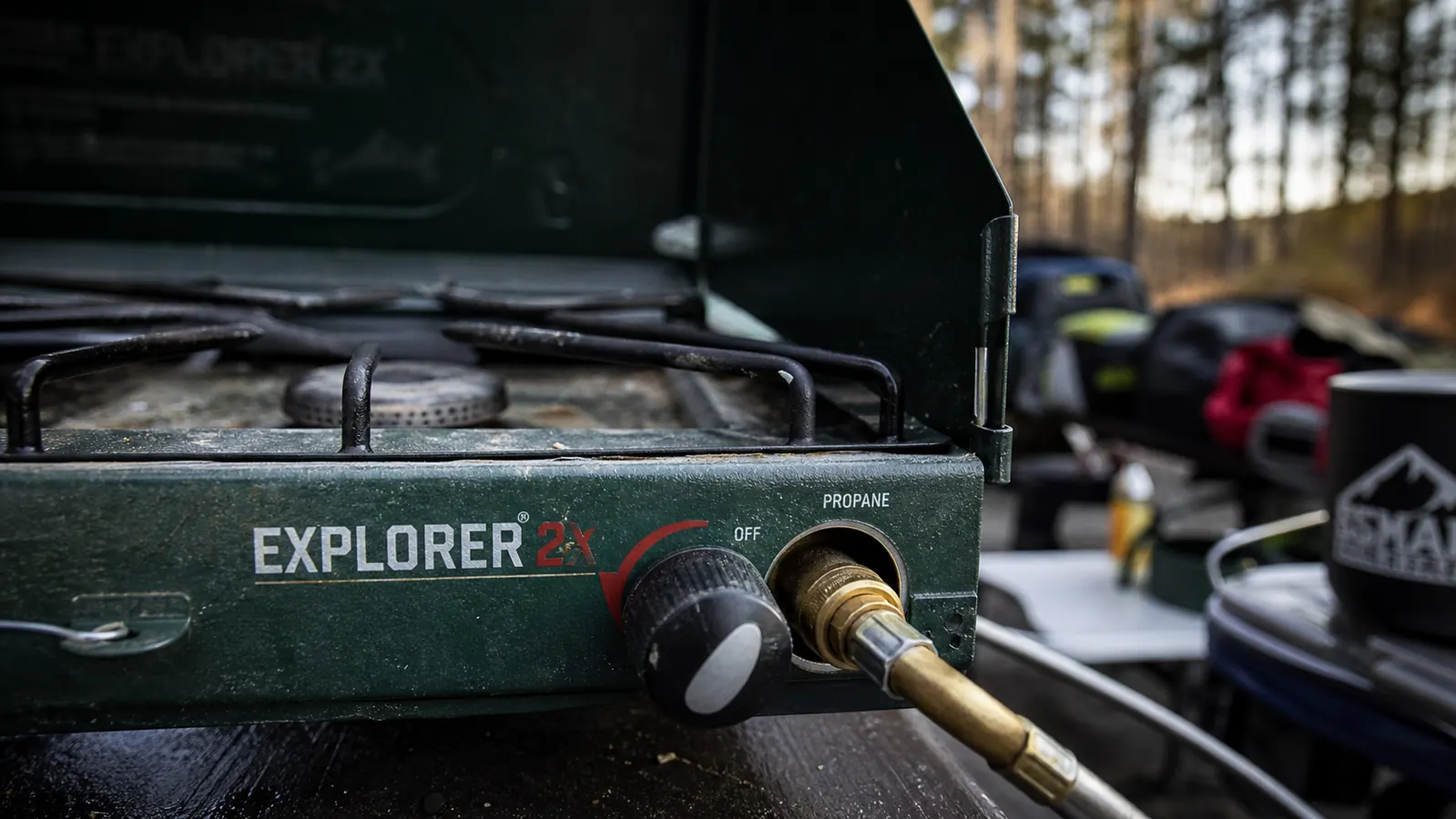 Camper cooking breakfast on the Coleman Triton in a forested campsite with two pans running simultaneously